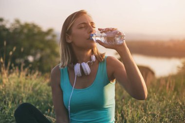 Egzersiz üzerinde otururken güzel sportif kadın içme suyu ile cityscape ve nehir behinde onu mat. Görüntü kasten tonda.