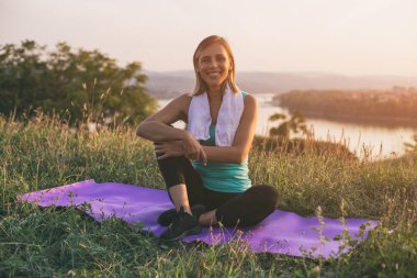 Güzel sportif kadın sittting egzersiz portresi ile cityscape ve nehir behinde onu mat. Görüntü kasten tonda.