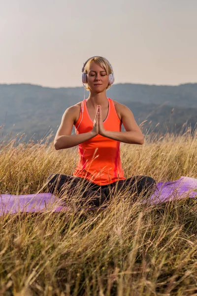 Padmasana 蓮華座 自然の中で瞑想とヘッドフォンの蓮華座でシッティングで美しい女性 画像は意図的にトーンダウンです — ストック写真