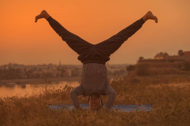 Man doing yoga on sunset with city view,Sirsasana/Supported Headstand.Toned image. clipart