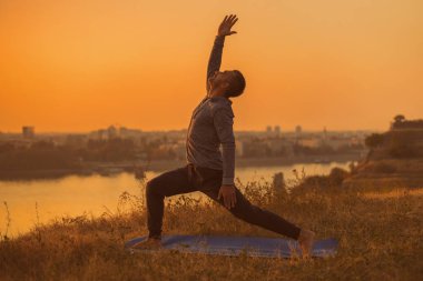 Şehir Manzaralı, savaşçı 1 poz/Virabhadrasana ı. tonlu görüntü günbatımı üzerinde yoga yapan erkek.