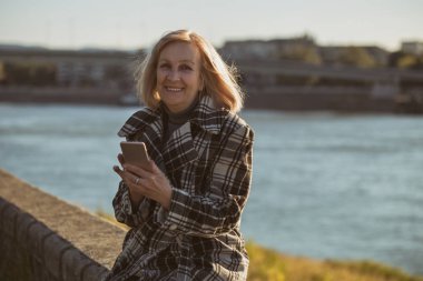 Telefonunuzun ve nehir kenarında otururken kadın kıdemli. Tonlu görüntü.