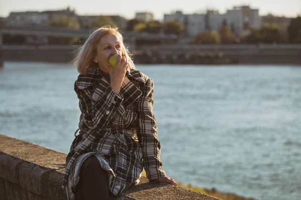 Senior Woman Enjoys Eating Apple While Sitting River Toned Image — Stock Photo, Image