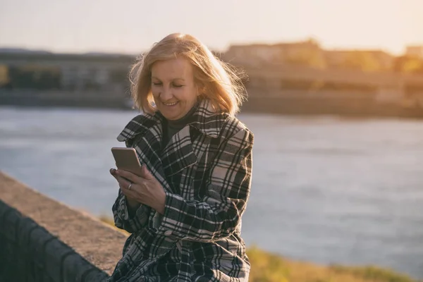 Ανώτερος Γυναίκα Χρησιμοποιώντας Τηλέφωνο Ενώ Κάθεται Δίπλα Στο Ποτάμι Πιο — Φωτογραφία Αρχείου