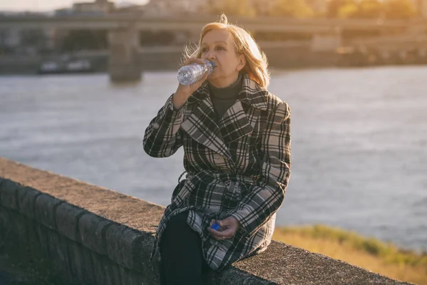 年配の女性は 川のそばに座って水を飲んでを楽しんでいます トーンのイメージ — ストック写真