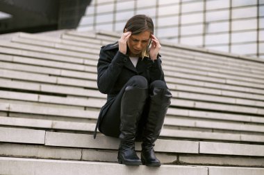Üzgün işkadını having baş ağrısı şehrin merdiven üzerinde otururken. Tonlu görüntü.