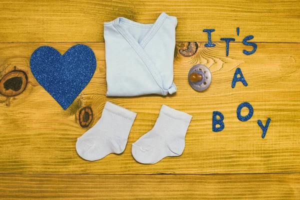 文字它是一个男孩与婴儿用品和心形的木桌上 色调照片 — 图库照片
