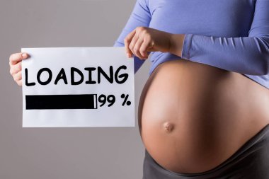 Gri arka plan üzerinde metin yükleme ile kağıt tutan hamile kadının yakın mide görüntüsü.