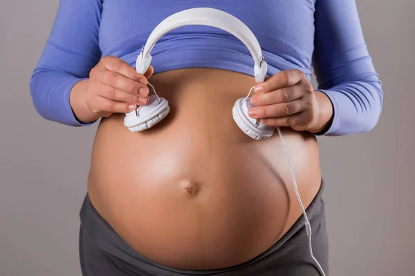 灰色の背景にヘッドフォンを持つ妊婦のクローズアップ胃の画像 — ストック写真