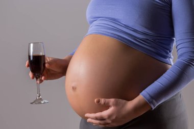 Image of pregnant woman drinking wine on gray background. clipart