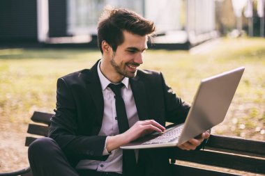 Şık işadamı açık havada otururken dizüstü bilgisayar kullanıyor. Tonlu görüntü.