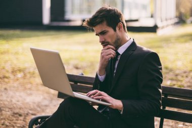 Endişeli iş adamı dışarıda otururken dizüstü bilgisayar kullanıyor. Görüntü ayarlı.