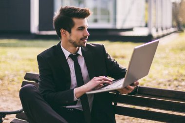 Şık işadamı açık havada otururken dizüstü bilgisayar kullanıyor. Tonlu görüntü.
