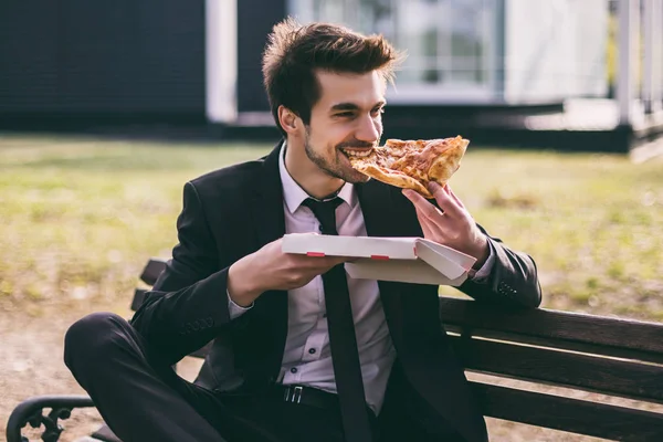 エレガントなビジネスマンは 屋外に座っている間 彼の昼休みにピザを食べることを楽しんでいます トーン画像 — ストック写真