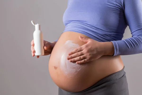 灰色の背景に彼女の胃に保湿剤を適用する妊娠中の女性の画像 — ストック写真
