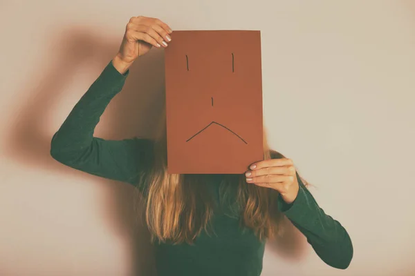 Depressed woman with sad face on paper standing alone in front of wall.Toned image.