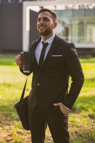 Elegant businessman on coffee break standing in the public park.Toned photo.