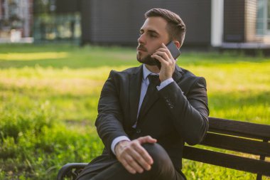 Endişeli iş adamı dışarıda otururken telefonu kullanıyor..