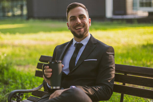 Elegant businessman enjoys drinking coffee while sitting outdoor.Toned image.