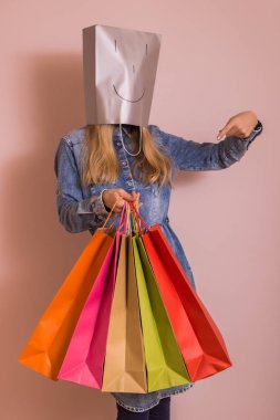 Duvarın önünde dururken kafasına torba ile alışveriş poşetleri tutan oyuncu kadın.