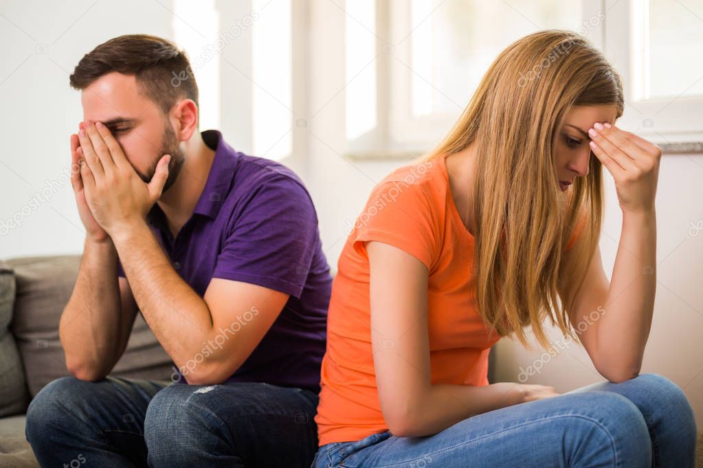 Angry wife and husband are having conflict while they sitting on sofa at their home.