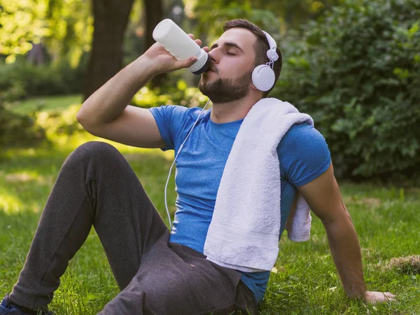 Handsome man with headphones  drinking water and resting after exercise in the park.