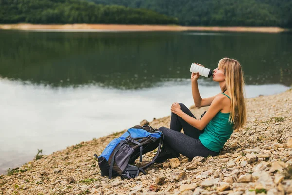 湖のそばに座っている間に水を飲む女性ハイカー — ストック写真