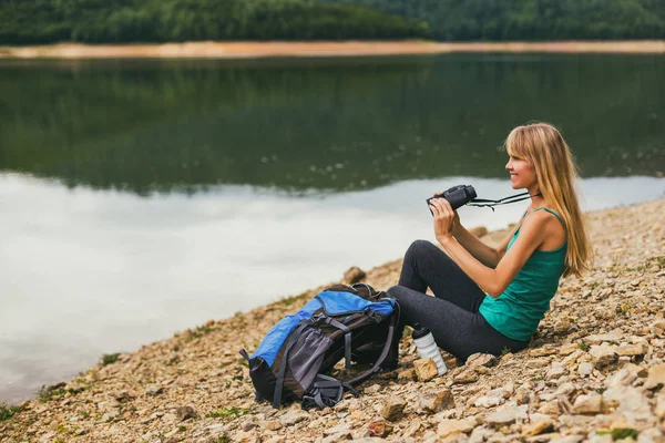 湖のそばに座っている間双眼鏡を使った女性ハイカー — ストック写真