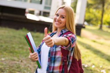 Açık havada dururken başparmağını gösteren güzel kız öğrenciportresi.