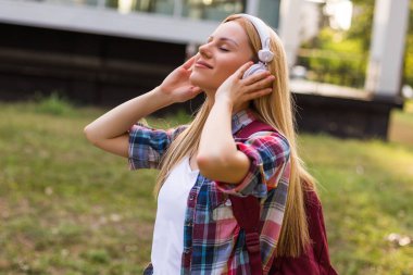 Female student with headphones enjoys listening music outdoor.