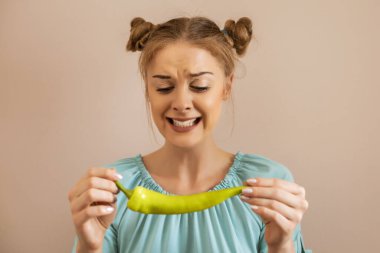 Şirin bir kadın elinde kırmızı biber tutarken yüzünü buruşturuyor..