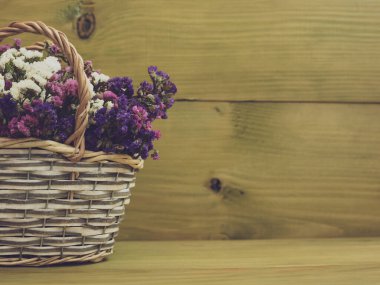 Tahta arka planda sepette kurumuş güzel çiçeklerin resmi.
