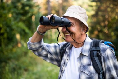 Doğa yürüyüşü yaparken dürbün kullanan sırt çantalı yaşlı adamın portresini kapat..