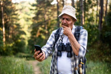 Worried senior hiker got lost and he is using mobile phone to find right direction while hiking in the nature.