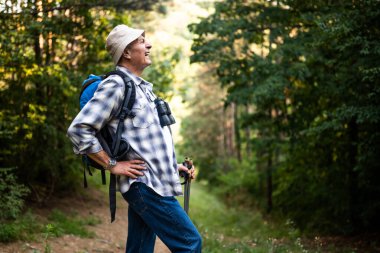 Sırt çantalı ve sırıklı yaşlı yürüyüşçünün doğa yürüyüşü yaparken sırtı ağrıyor..