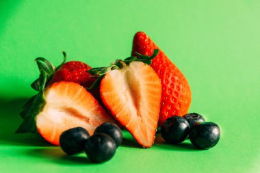 Yeşil arka planda taze kesilmiş çilek ve taze yaban mersini. Sağlıklı gıda konsepti.