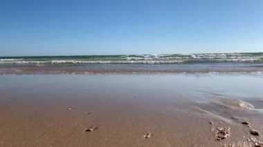 Dalgalar kıyıda mavi gökyüzü ve kumlar ön planda