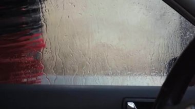 Otomatik araba yıkama, temizlik fırçaları arabayı yıkayıp cilalarken, yan camı kirletirken. Pencereden aşağı süzülen su damlaları. Araba yıkama