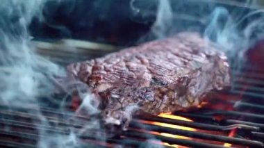 Kavrulmuş et bifteği, baharat ve otlarla birlikte BBC ızgarasında yanan kömürler, alevler ve ağır çekimde duman. Izgara çizgili sulu biftek piknik kutlaması için hazır. Barbekü ızgarası