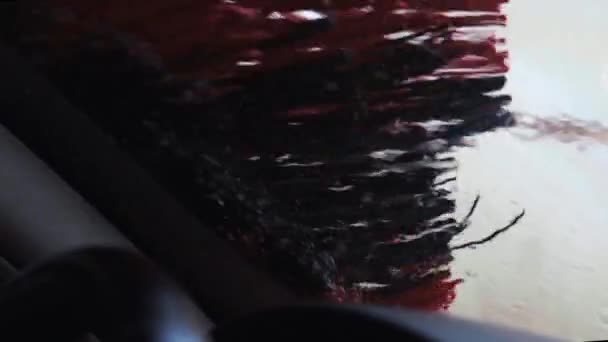自动洗车过程,长红色和黑色刷子旋转和清洗汽车挡风玻璃.水滴从窗户流下来.食环署洗车行动 — 图库视频影像