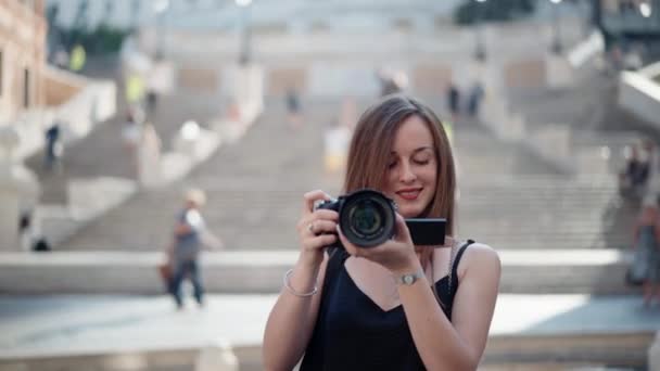 Atrakcyjny uśmiechnięty fotograf trzymający jej czarny aparat cyfrowy i robiący niesamowite przełomowe zdjęcia. Kreatywna dziewczyna szuka najlepszej kompozycji fotograficznej, nagrywa wspomnienia miasta przed kamerą — Wideo stockowe