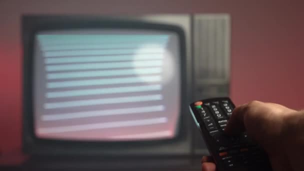 Stará klasická televize na aukčním trhu, detailní záběr z ruky, držící dálkové ovládání a mačkající tlačítka pro přepínání kanálů. Starožitný retro TV s blikající obrazovkou na tmavočerveném pozadí — Stock video