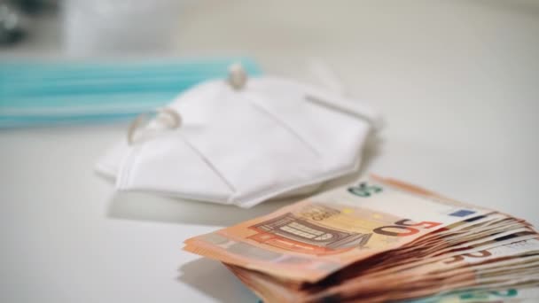 Een stapel eurobankbiljetten op witte achtergrond naast de beschermende medische maskers en een aantal verschillende dure pillen, capsules en steriele injectieflacons. Verhoging van prijzen en ontwikkeling van — Stockvideo