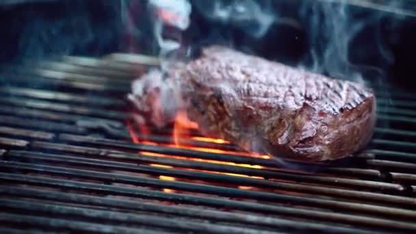Chef using cooking metal tongs for turning delicious juicy meat steak roasting on metal bbq grid, fried beef steak on burning fire with smoke, picnic preparation. Barbecue party outdoors — Stock Video