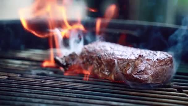 美味的多汁牛肉牛排烤与烟和燃烧的火焰在bbq格栅在火盆，烧烤烧烤在室外慢动作。烤和煎生肉牛排，上有香料和香草 — 图库视频影像