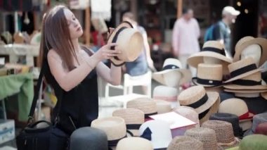 Panama şapkasını yerel el sanatları pazarında deneyip aynaya bakan şık bir kız. Farklı türde ve kafa malzemeleriyle dolu bir market tezgahı, turistleri çeken renkli çeşitlilikler. Yaz