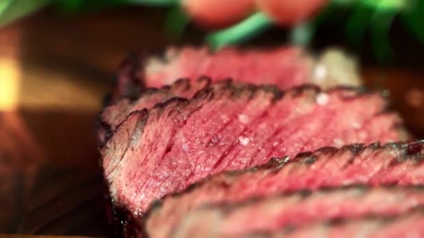 Deliciosos trozos de carne asada a la parrilla mediana rara carne de res en la tabla de madera, sal y pimienta condimento que cae en la carne asada jugosa. Filete de ternera al vapor con sangre servido en un restaurante de lujo — Vídeo de stock