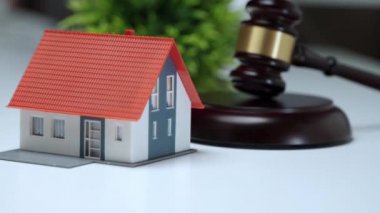 Mülk müzayedesinde ev alma süreci, yargıç kararı ve tokmak çakma. Ev modeli ortadan kayboluyor ve ahşap tokmağın yanındaki masaya yığınla para düşüyor. Gayrimenkul, yeni mal sahibi ve