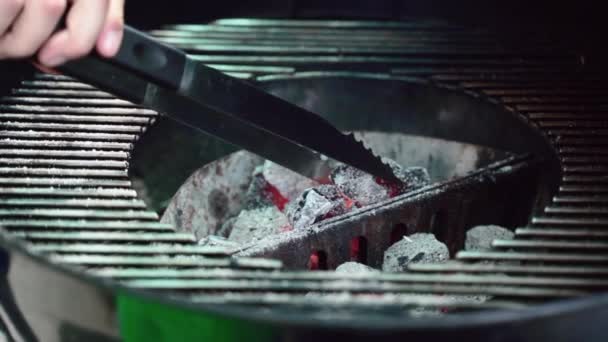 Carvão quente vermelho na moderna grelha braseiro portátil. Chamas e brasas vermelhas no ar. Carvão de laranja saindo em grelha grelha, chef usando pinças de cozinha de metal para misturar lascas de queima de madeira — Vídeo de Stock