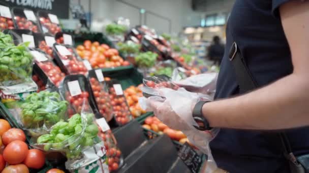MILÁN, ITALIA - 23 DE MAYO DE 2020: Hombre con guantes protectores eligiendo tomates frescos en el departamento de comestibles en el supermercado de Milán durante el brote pandémico de covid-19, abasteciendo verduras y frutas en — Vídeos de Stock